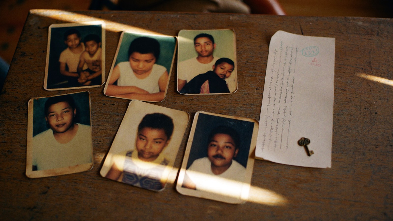 Fotografias antigas de uma família negra brasileira espalhadas sobre uma mesa de madeira, ao lado de uma carta manuscrita dobrada e uma chave antiga